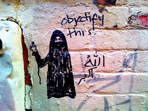 (woman in hijab with partial face veil, middle finger raised in defiance.